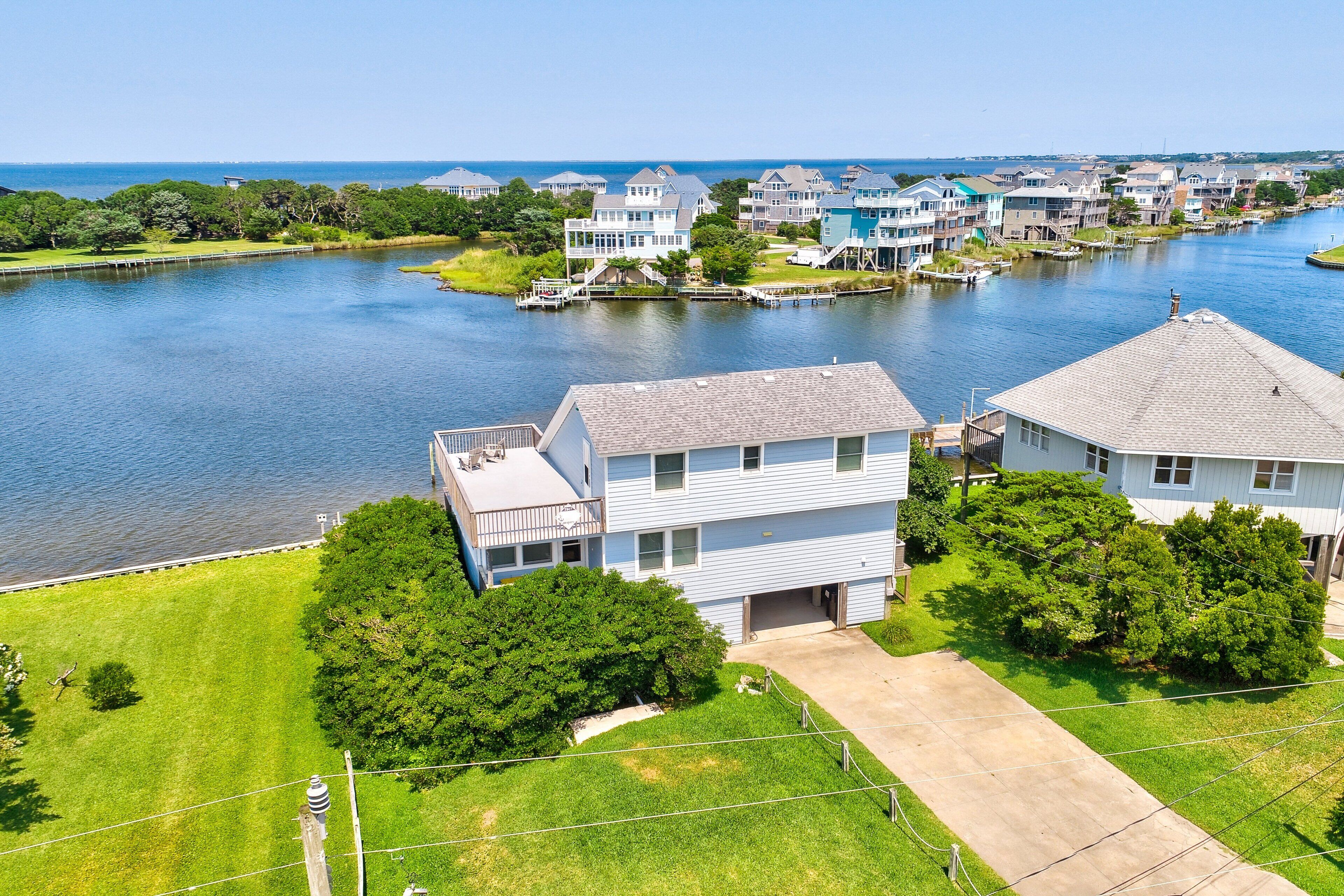 A residential area with houses along a river, featuring a grassy lawn and a dock.