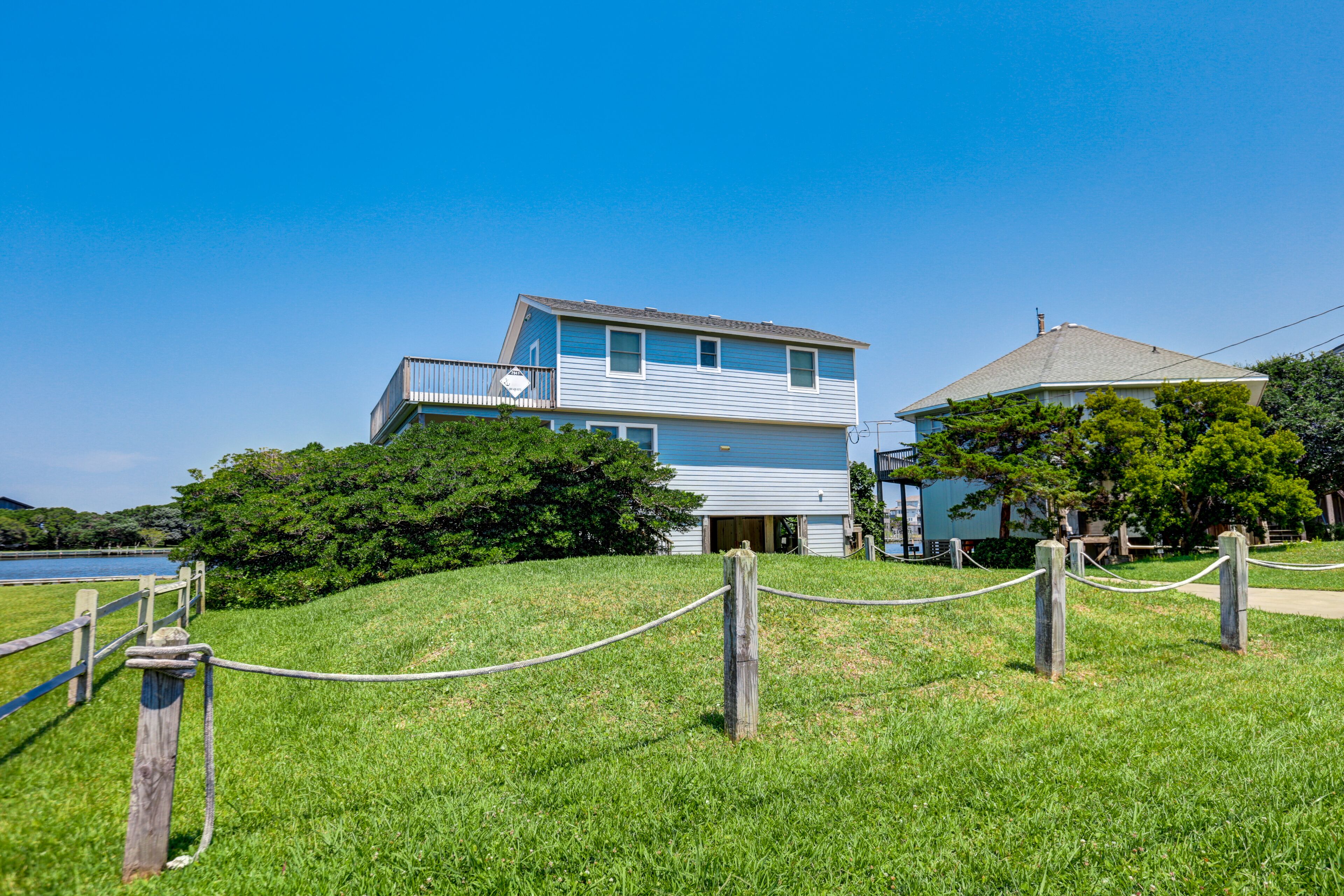 A two-story house with a balcony, surrounded by a grassy area and a wooden fence.