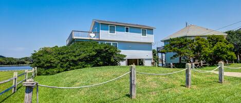 A two-story house with a balcony, surrounded by a grassy area and a wooden fence.