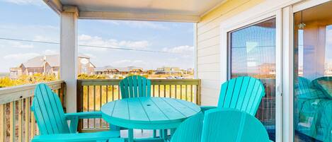 A covered balcony with turquoise Adirondack chairs and a small round table.
