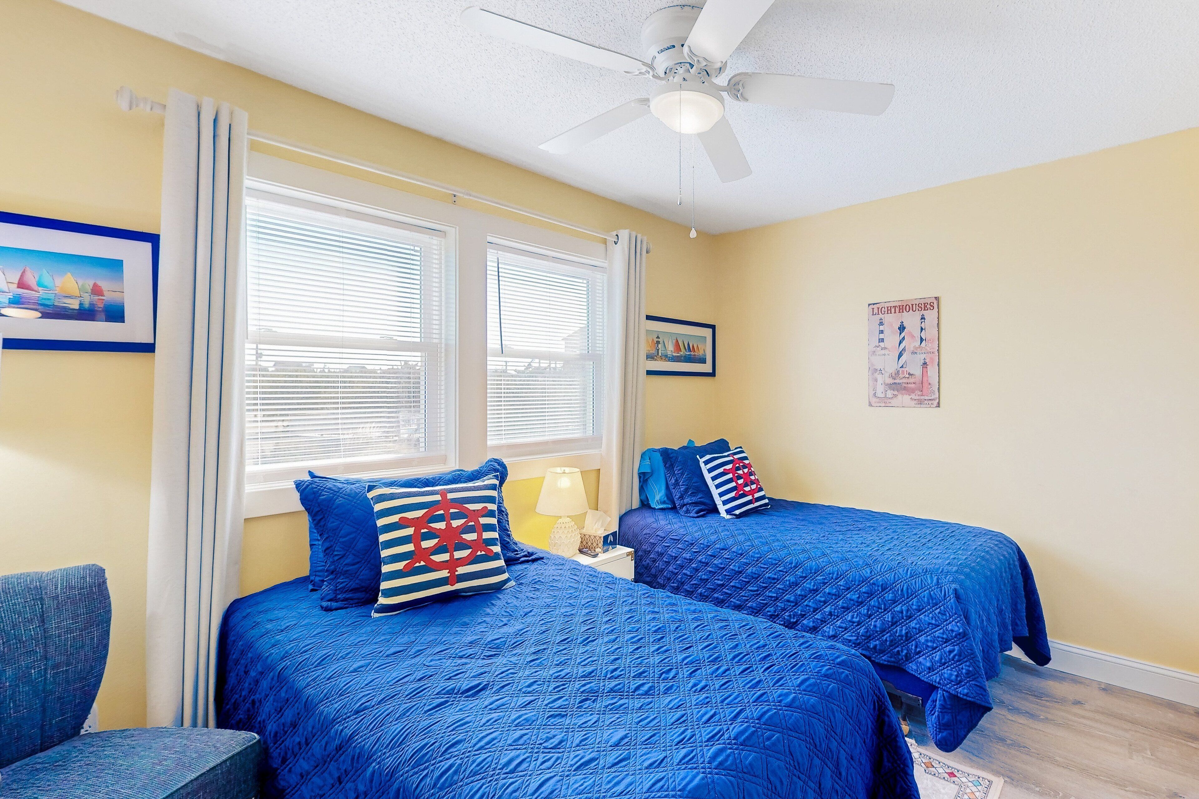 A bedroom with two beds, a ceiling fan, and a window with blinds.