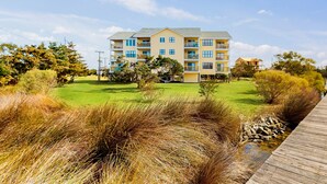 Un edificio residencial de varios pisos con balcones, un césped y un paseo marítimo de madera.