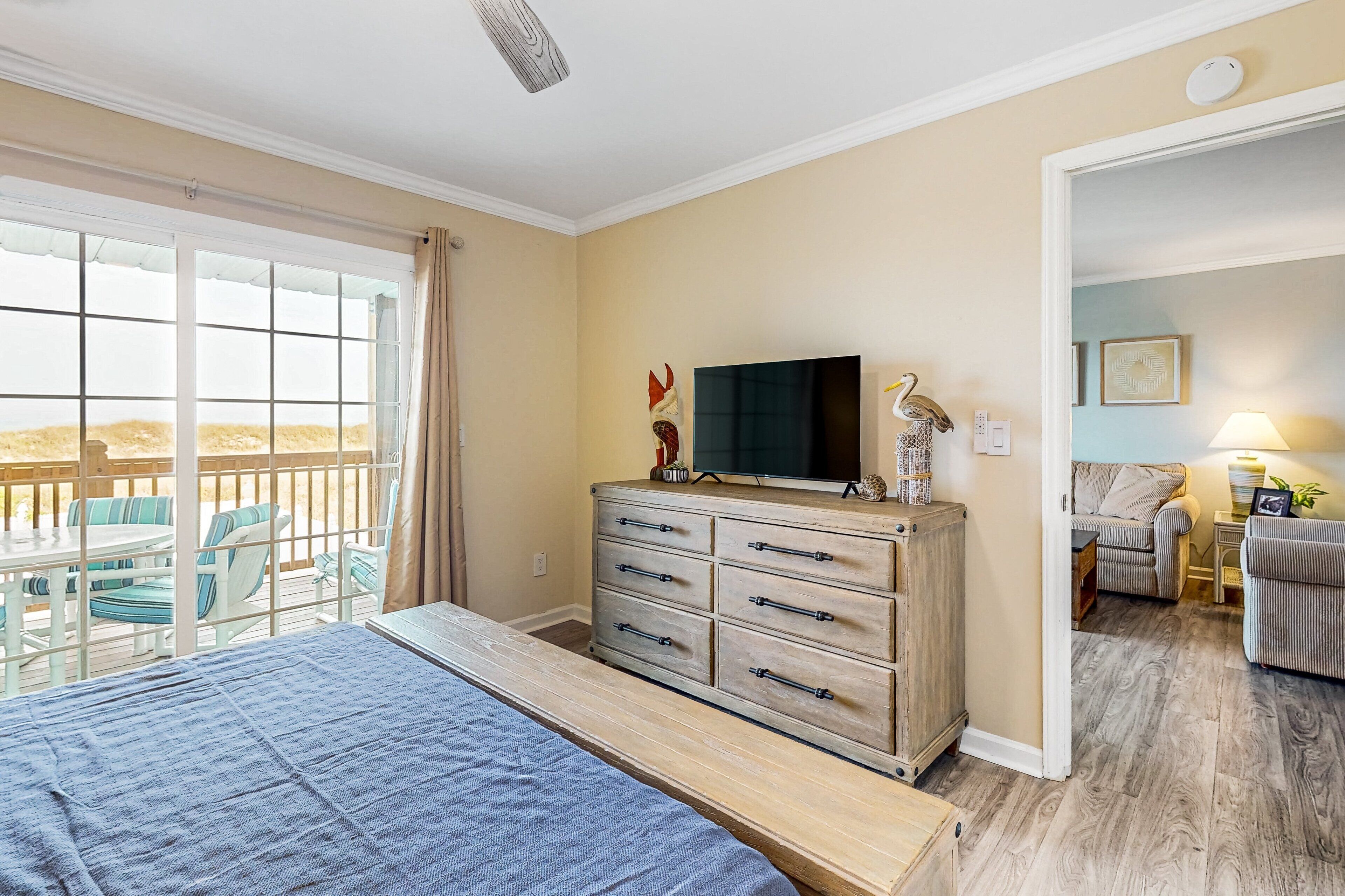 Ein Schlafzimmer mit Bett, Kommode, Fernseher und einem Balkon mit Gartenmöbeln.