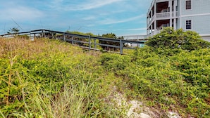 A coastal building with a balcony, surrounded by dense vegetation and a wooden bridge.