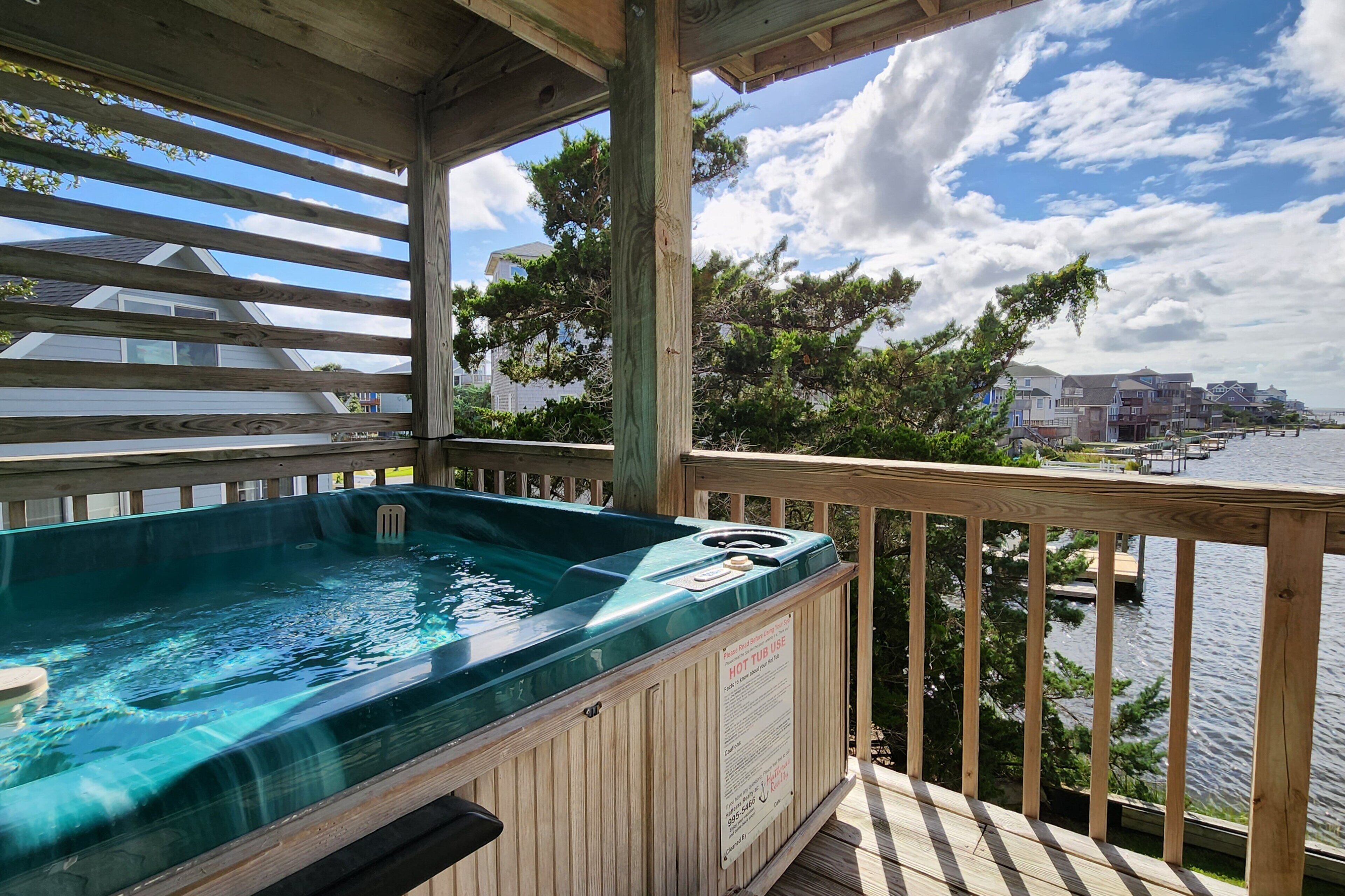 A hot tub on a wooden deck with a view of a waterfront and buildings in the background.