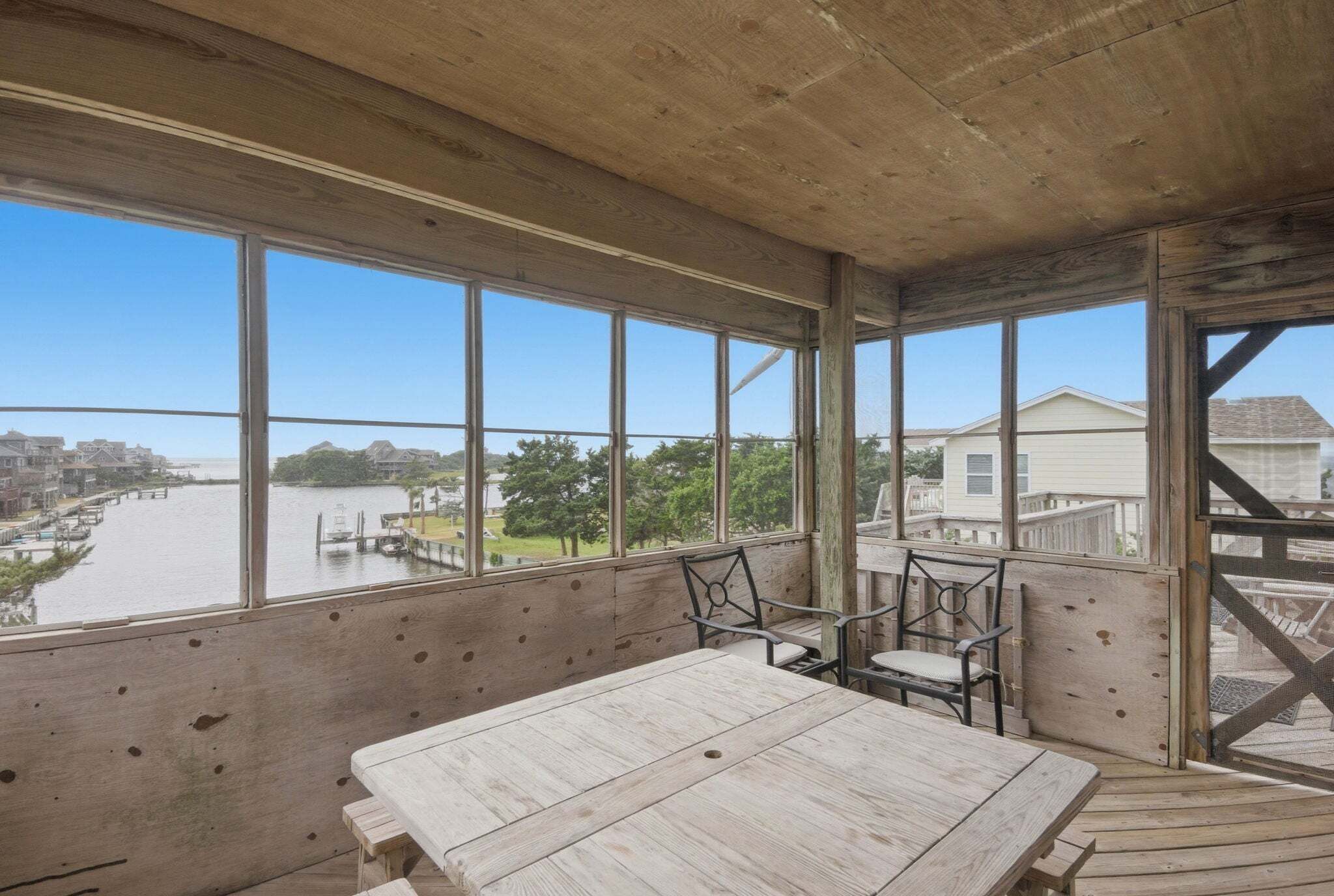 A wooden deck with a table and chairs, overlooking a river and houses.