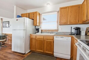 A compact kitchen with wooden cabinets, a white refrigerator, a dishwasher, and a coffee maker.