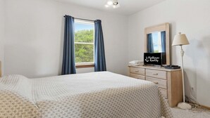 Quarto com cama, penteadeira, espelho, ventilador de teto e janela com cortinas.