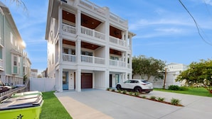 A multi-story residential building with a white exterior, multiple balconies, and a car parked in the driveway. - Oceanview home with close proximity to the beach, AC, W/D, & deck (Carolina Beach)