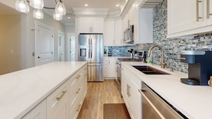A modern kitchen with white cabinetry, stainless steel appliances, and a tiled backsplash. - Oceanview home with close proximity to the beach, AC, W/D, & deck (Carolina Beach)