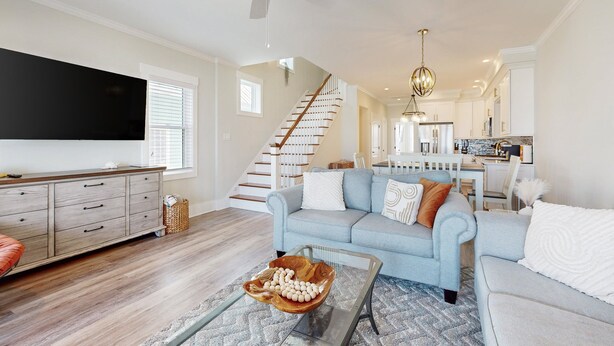A spacious living room with a large flat-screen TV, a light blue sofa, a wooden coffee table, and a staircase leading to the upper floor. - Oceanview home with close proximity to the beach, AC, W/D, & deck (Carolina Beach)
