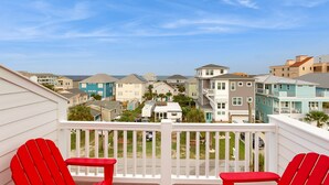 A balcony with red chairs, overlooking a residential area with various houses and a clear blue sky. - Oceanview home with close proximity to the beach, AC, W/D, & deck (Carolina Beach)