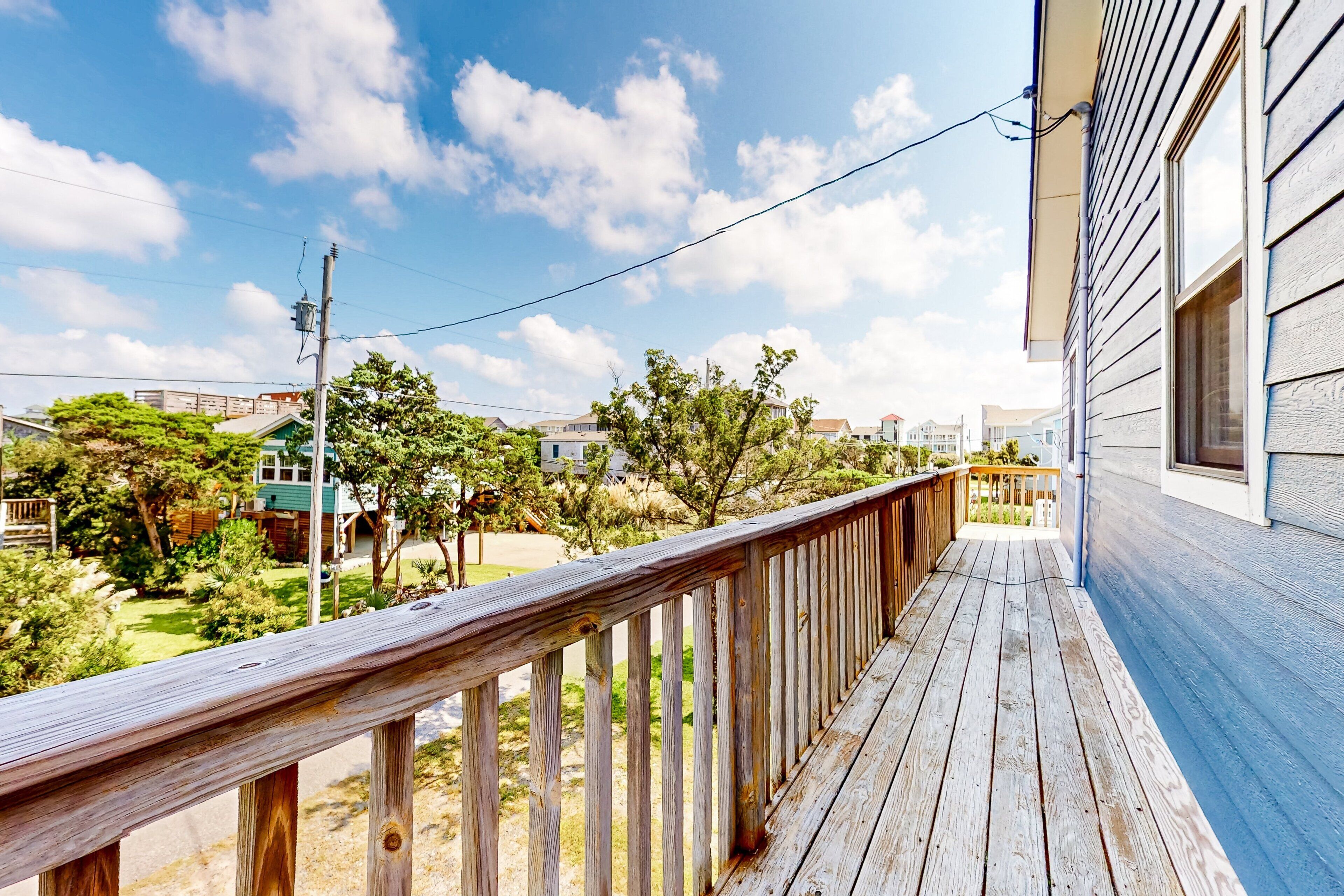 Um deck de madeira com guarda-corpo, com vista para uma área residencial com casas e vegetação.