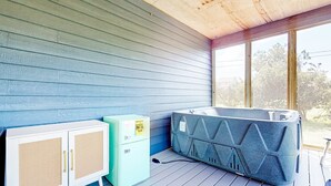 Una habitación con techo de madera, pared azul, un armario blanco con un refrigerador pequeño y una bañera de hidromasaje.