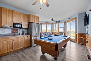A pool table in a room with wooden cabinets, a microwave, and a refrigerator.