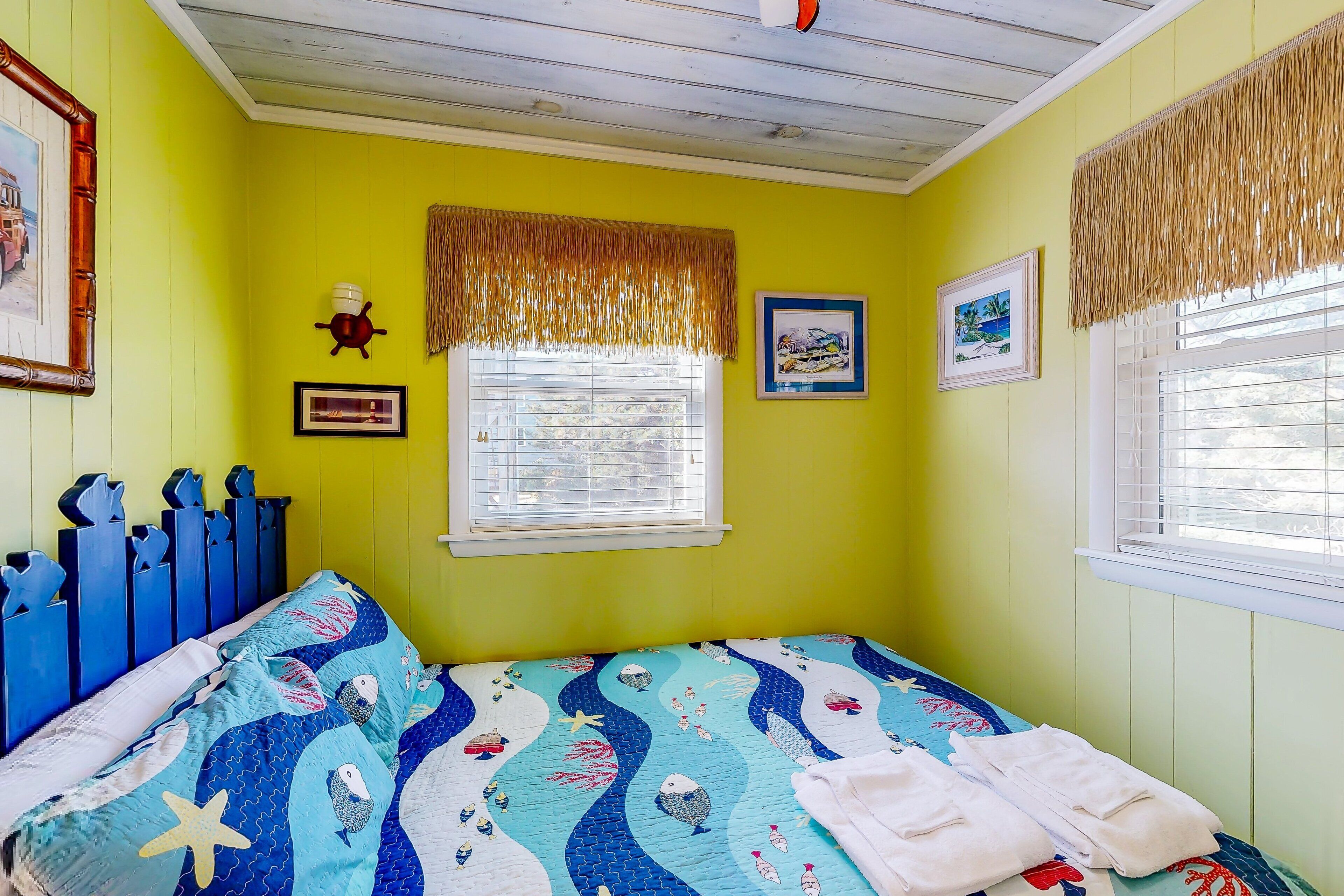 A bedroom with a bed, a window with blinds, a wall clock, and a framed picture.