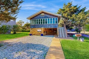 A two-story building with a large windowed front, a wooden deck, and a gravel driveway.