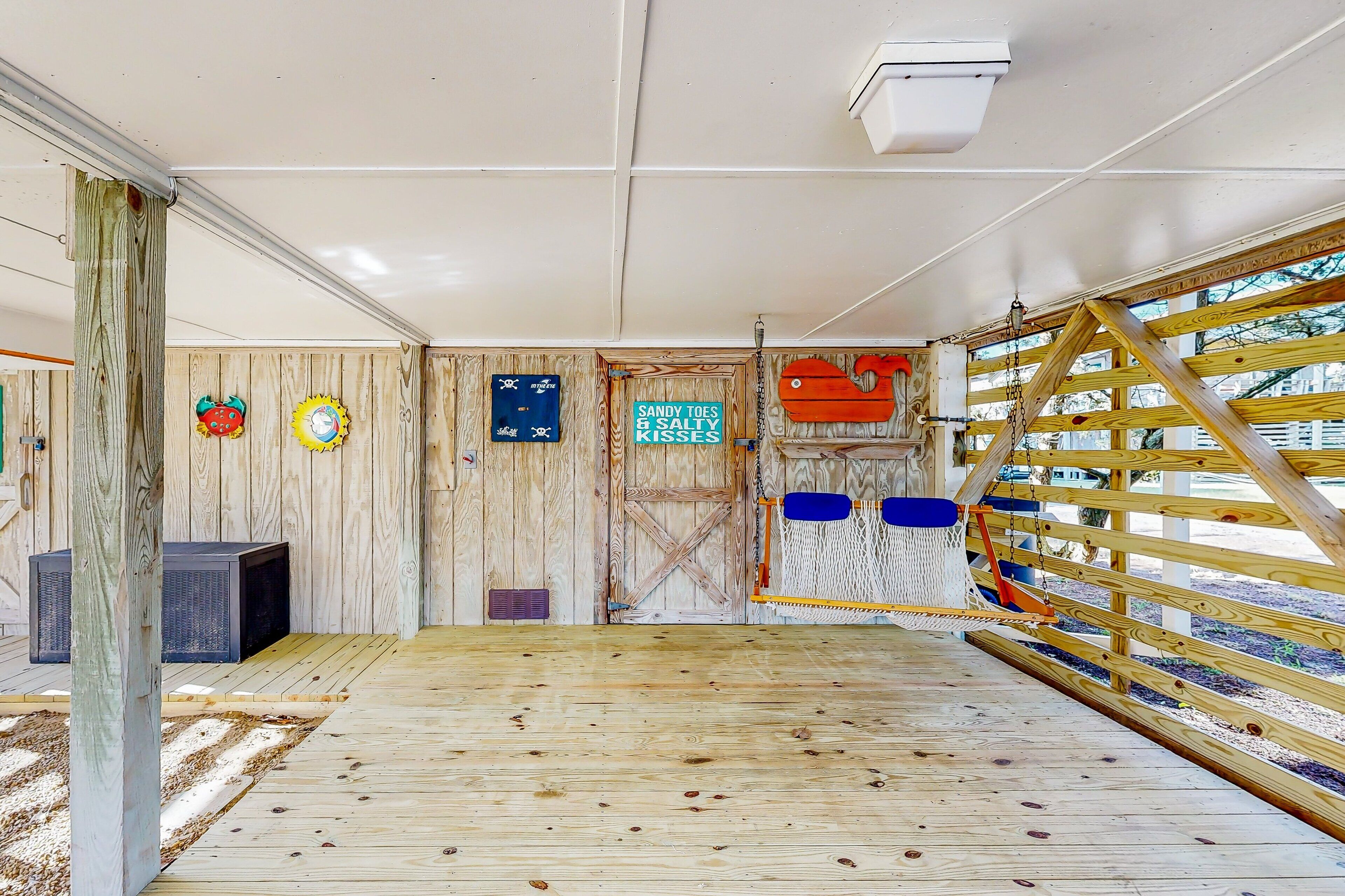 A wooden interior with a wooden floor, a door with a sign, and a view through a wooden fence.