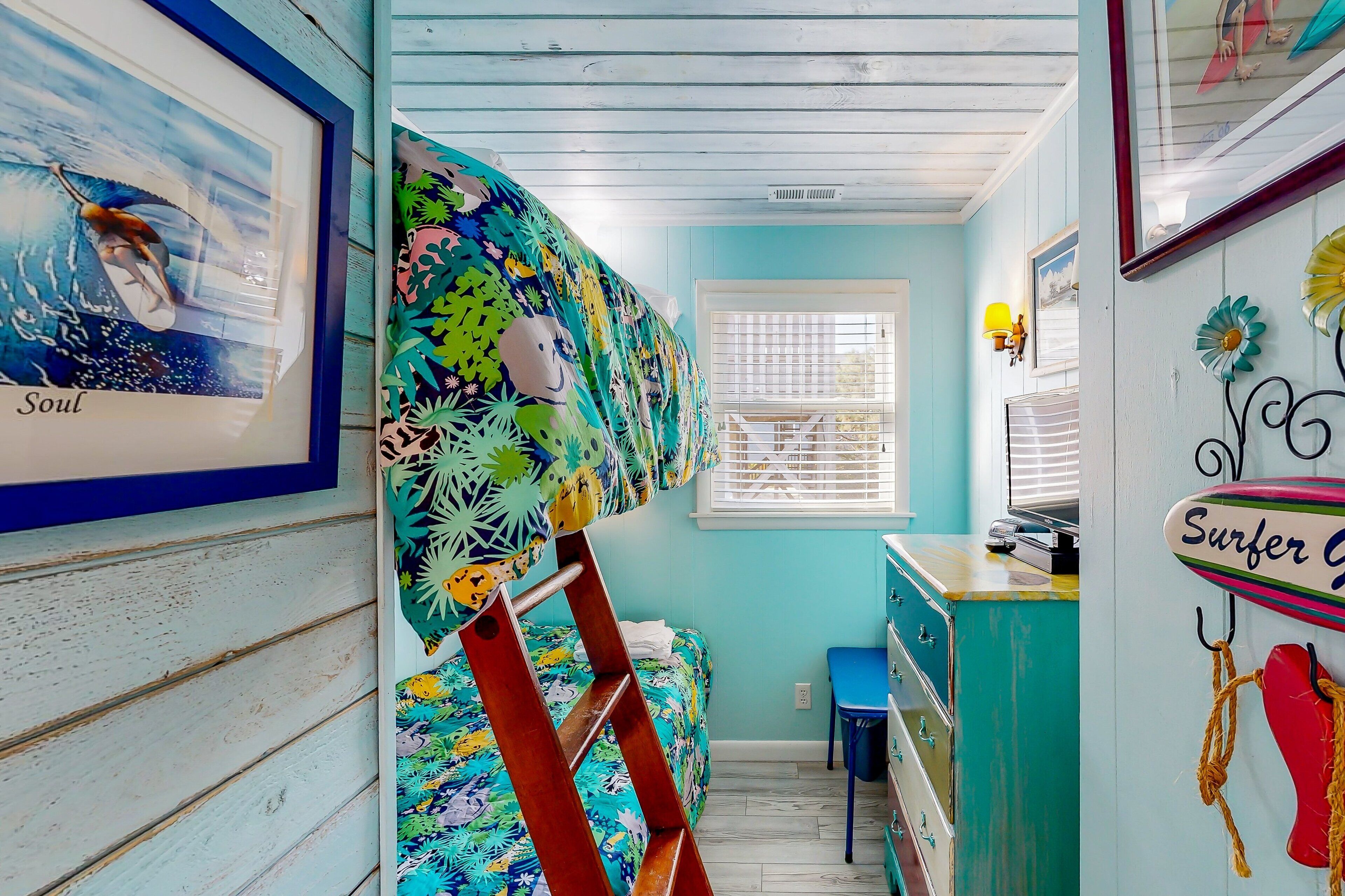 A room with a bunk bed, a desk, a chair, and a window with blinds.