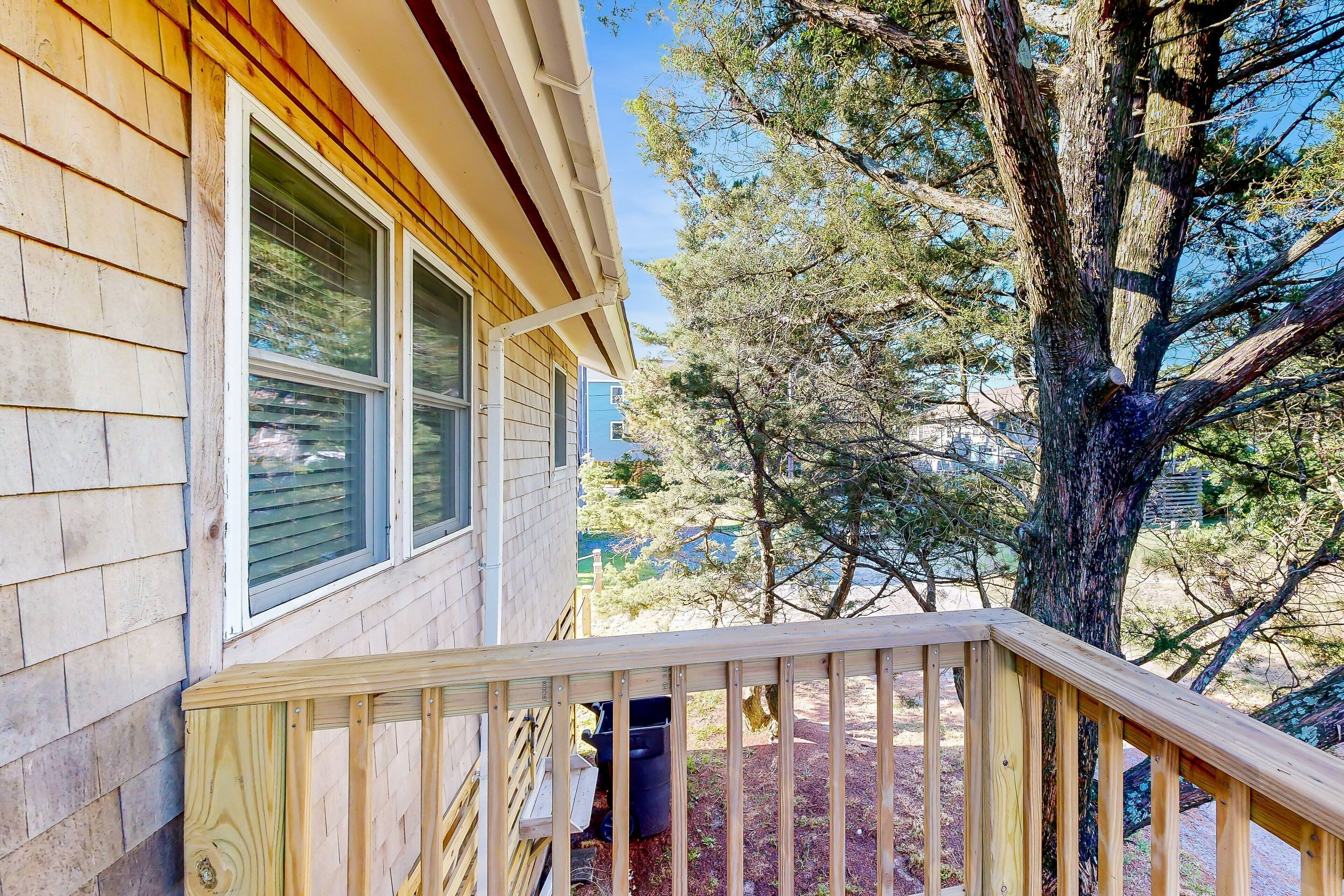 A wooden house with a porch and a large tree in the background.