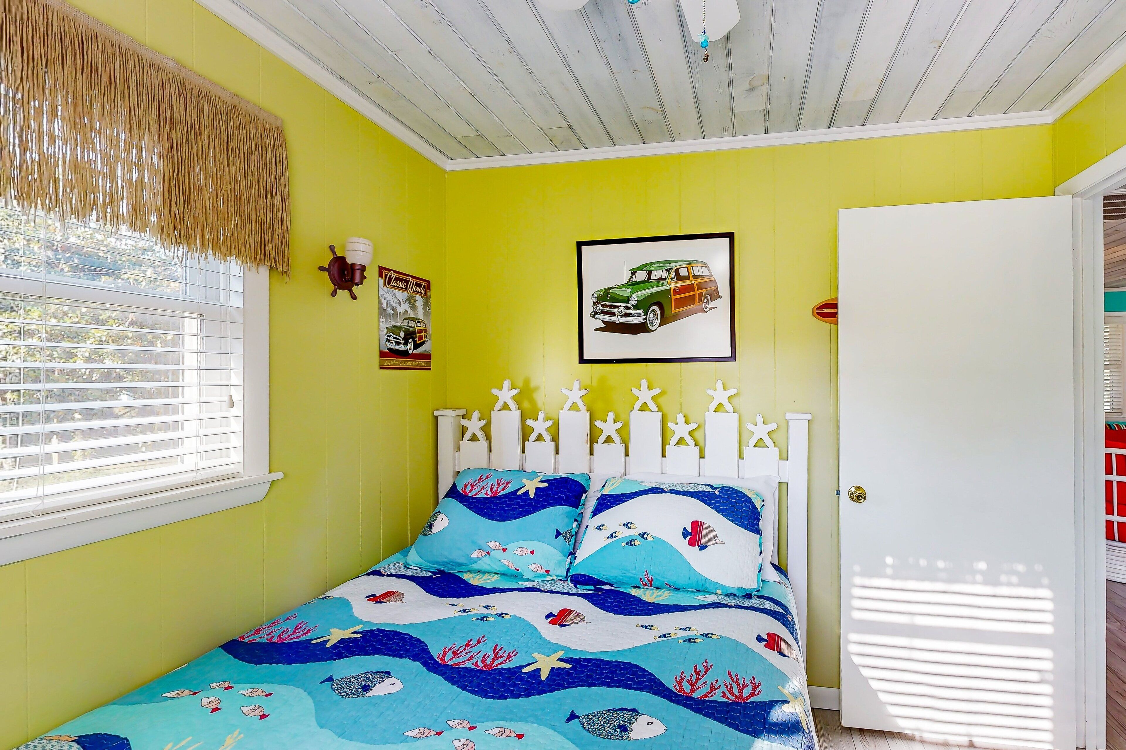 A room with a bed, a window with blinds, a door, and a wall with a picture.
