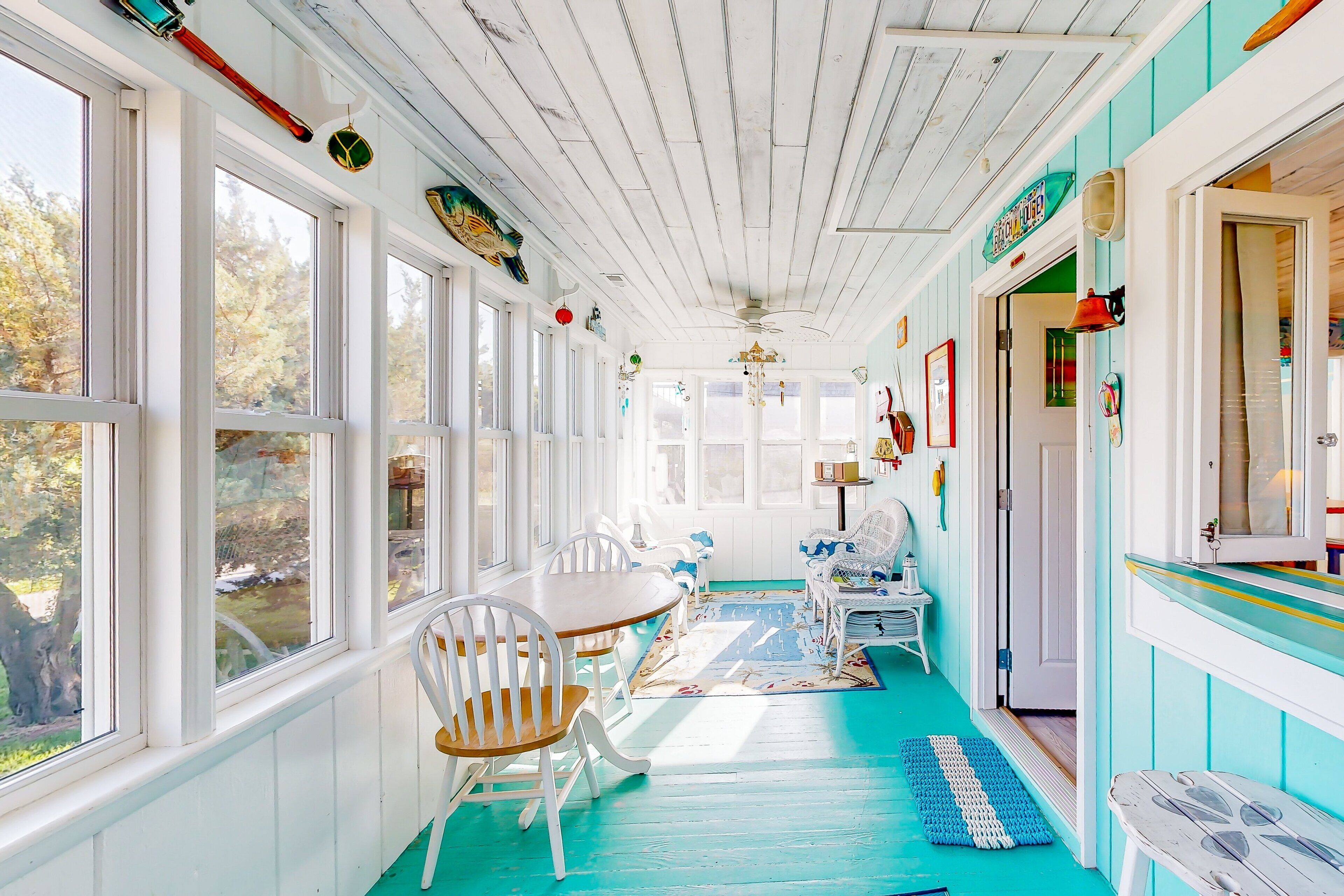 Una stanza luminosa con soffitto in legno, pareti bianche e pavimento color petrolio. Si vede un tavolo da pranzo con sedie, un tavolino bianco e una panca.