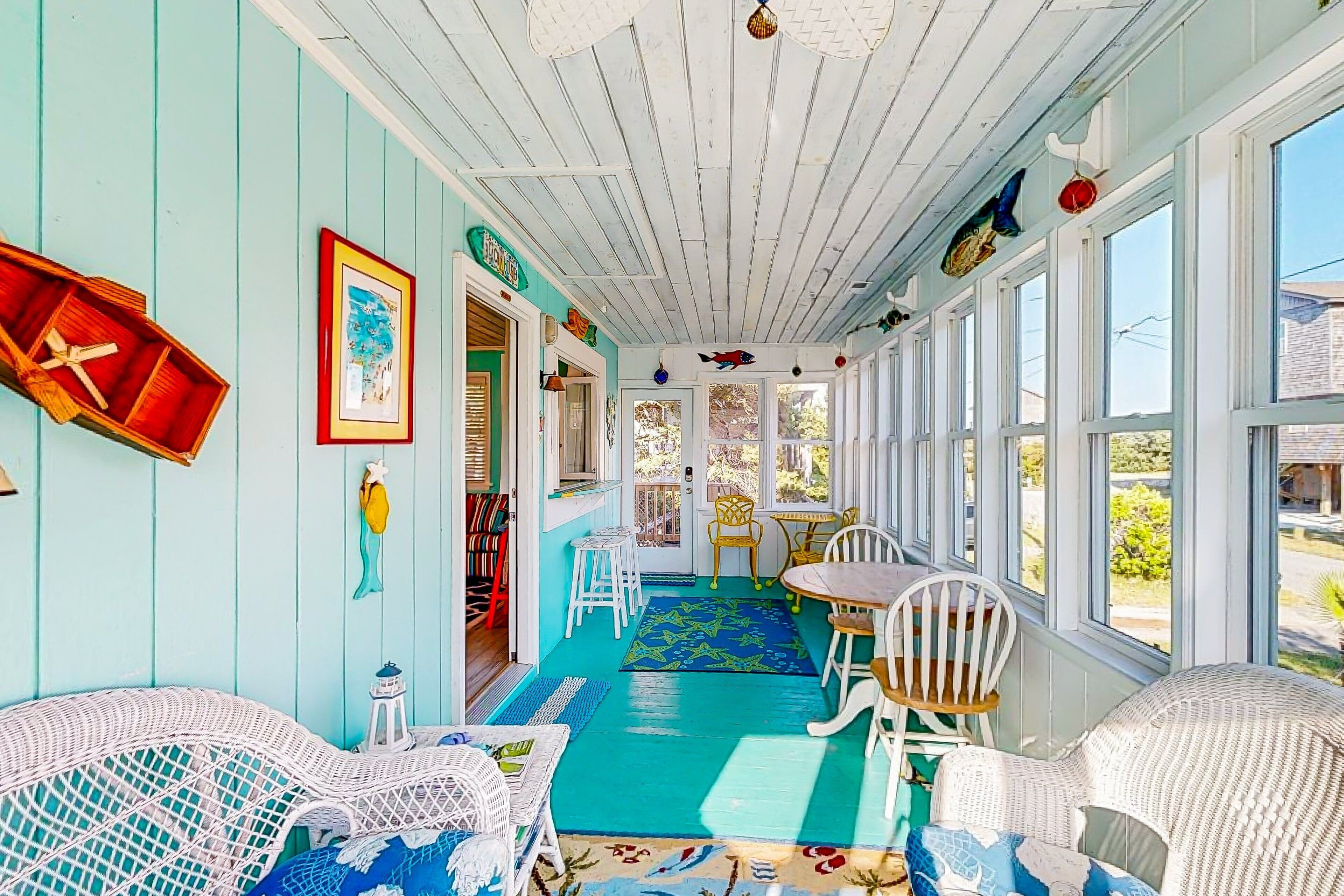 A sunroom with a blue floor, white wicker furniture, and a view of the outside.