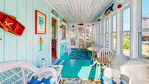 Un solárium con piso azul, muebles de mimbre blanco y vistas al exterior.