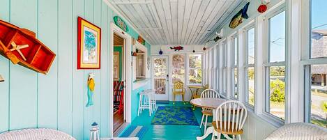 A sunroom with a blue floor, white wicker furniture, and a view of the outside.