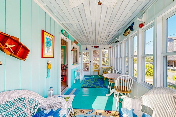 A sunroom with a blue floor, white wicker furniture, and a view of the outside.