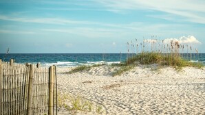 A sandy beach with a wooden fence and tall grasses in the foreground, leading to the ocean. - Historical Riverfront Condo in Historic District, Highly Walkable Locale (Wilmington)