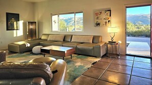 Una sala de estar con un sofá modular, una mesa de centro, una lámpara y vistas a las montañas a través de una ventana.