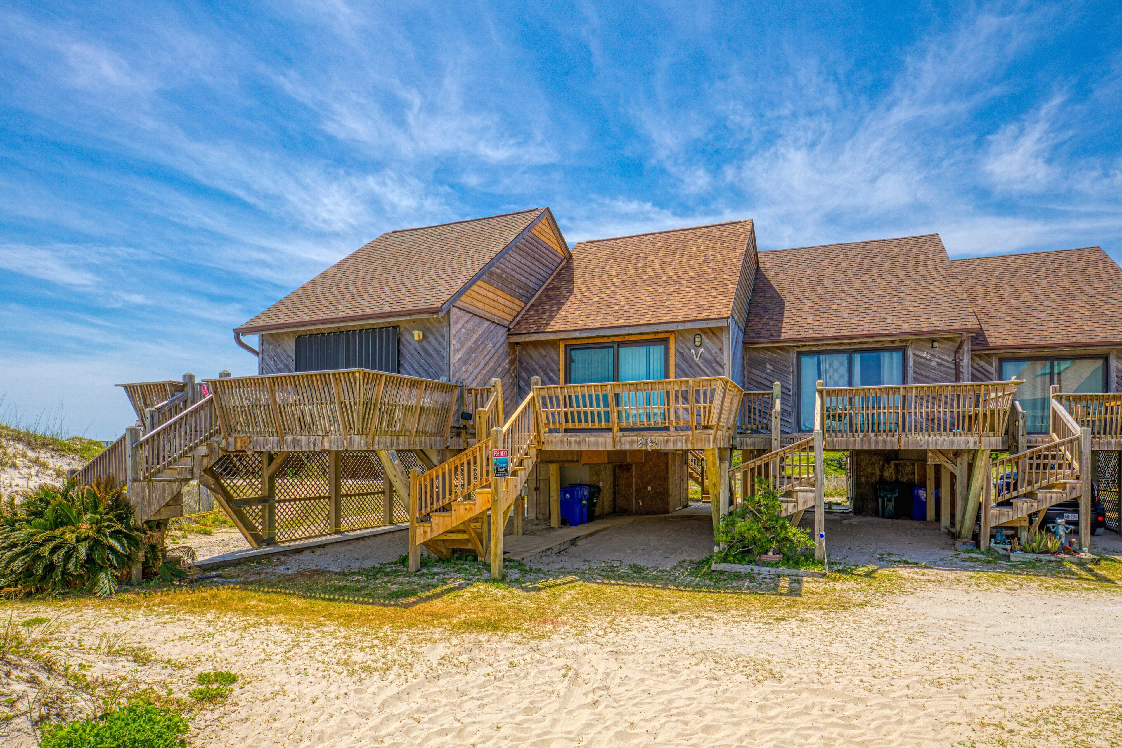 A beachfront property with a wooden deck, multiple levels, and a sandy beach area.