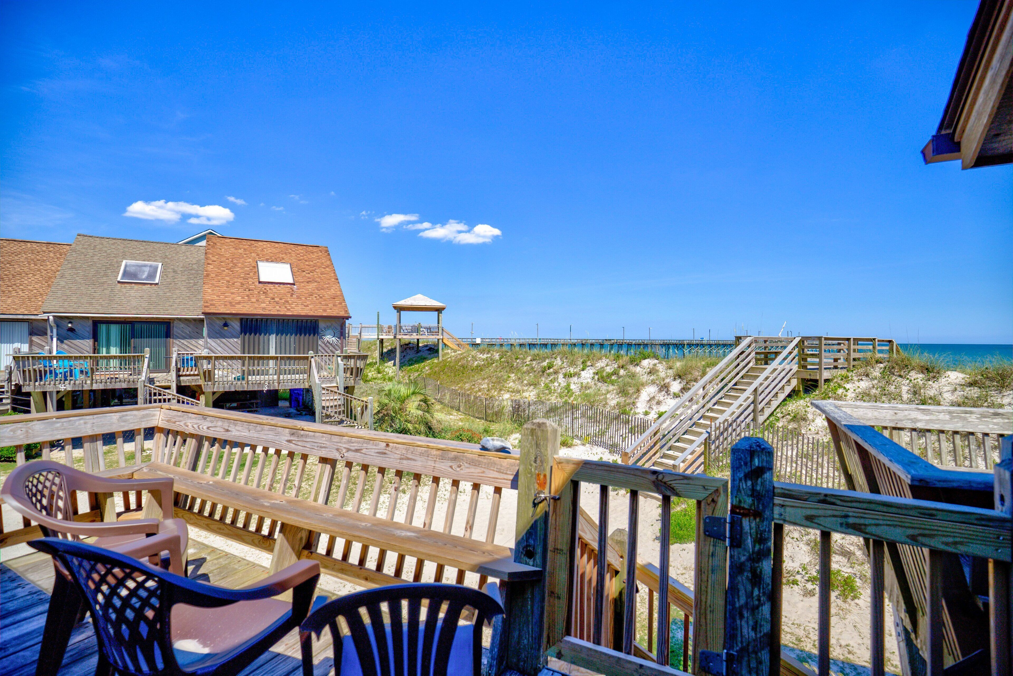 A wooden deck with chairs and a gazebo overlooking a beach.