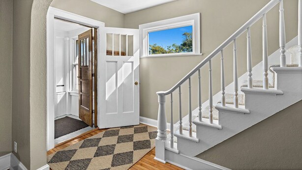 A hallway with a wooden floor, a checkered rug, a white door, and a staircase with white railings. - Newly Renovated and Welcoming 3-bedroom house in Superior (Superior)