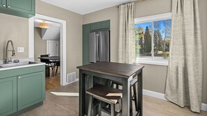 A kitchen with green cabinets, a dark wooden table, and a view of a garden through a window with beige curtains. - Newly Renovated and Welcoming 3-bedroom house in Superior (Superior)