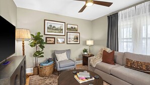 A living room with a sofa, armchair, coffee table, and TV. There are framed pictures on the wall, a ceiling fan, and a window with curtains. - Newly Renovated and Welcoming 3-bedroom house in Superior (Superior)