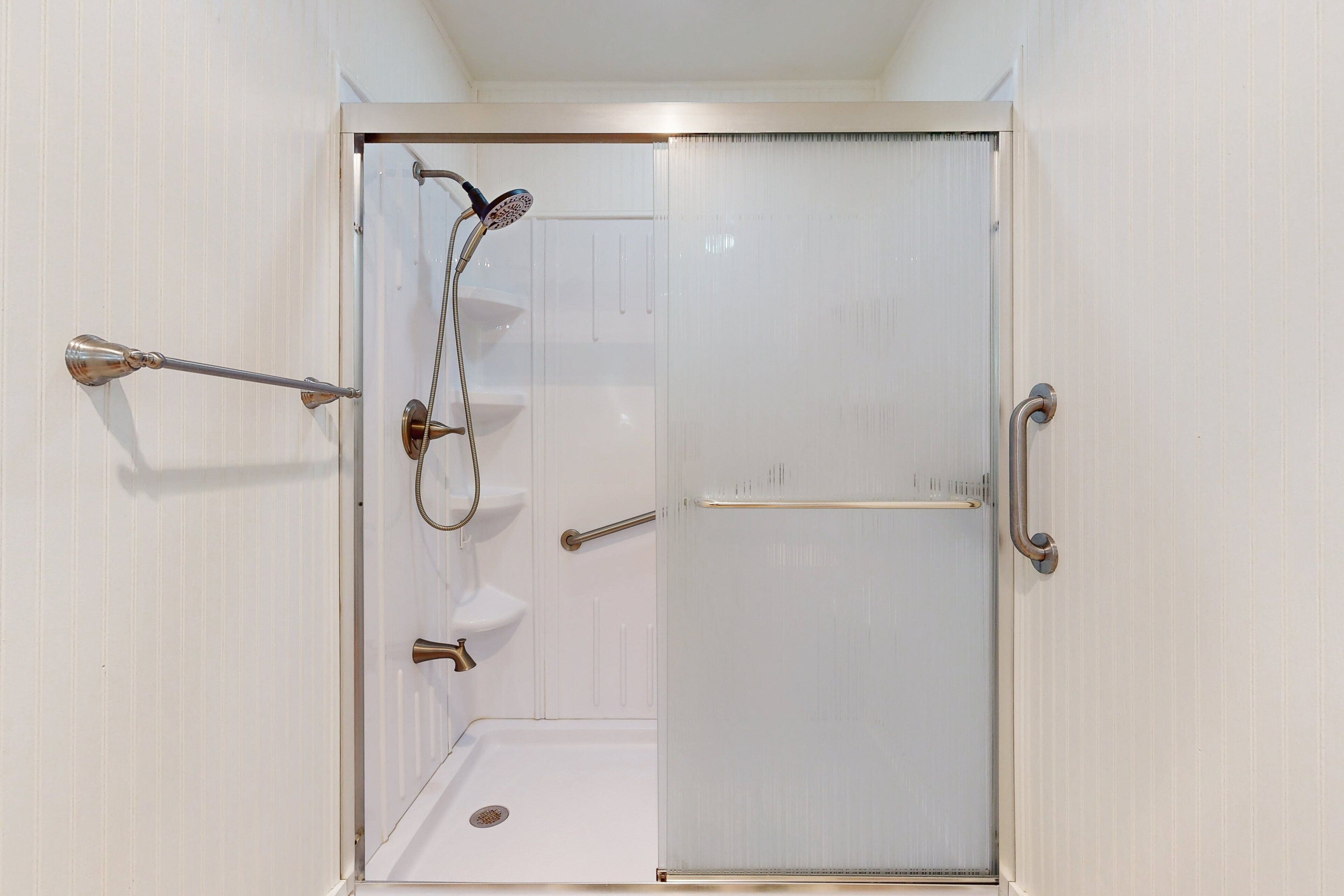Eine gläserne Dusche mit Handbrause, Duscharmatur und Auszugshahn.