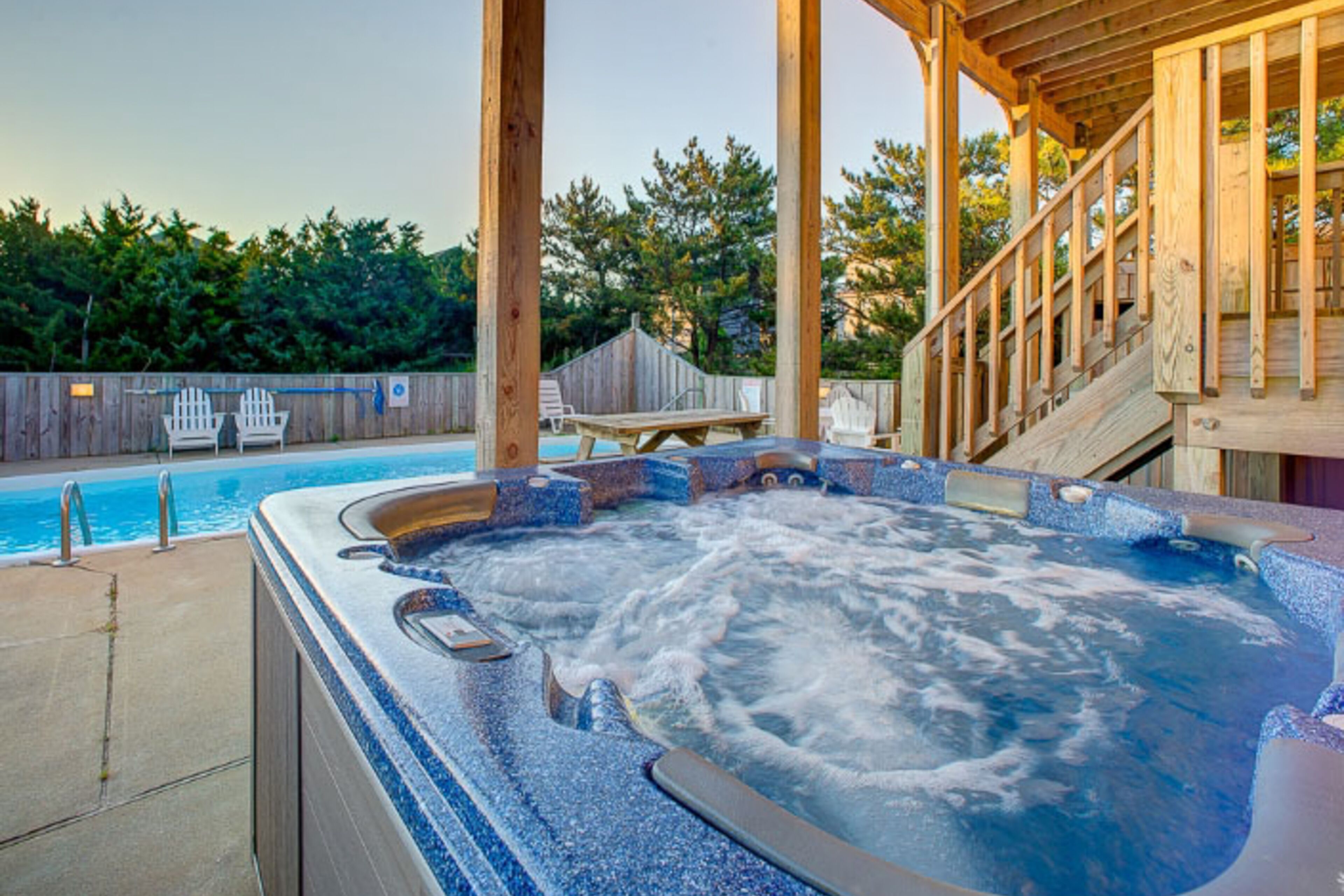 A hot tub with a wooden deck and a pool in the background.