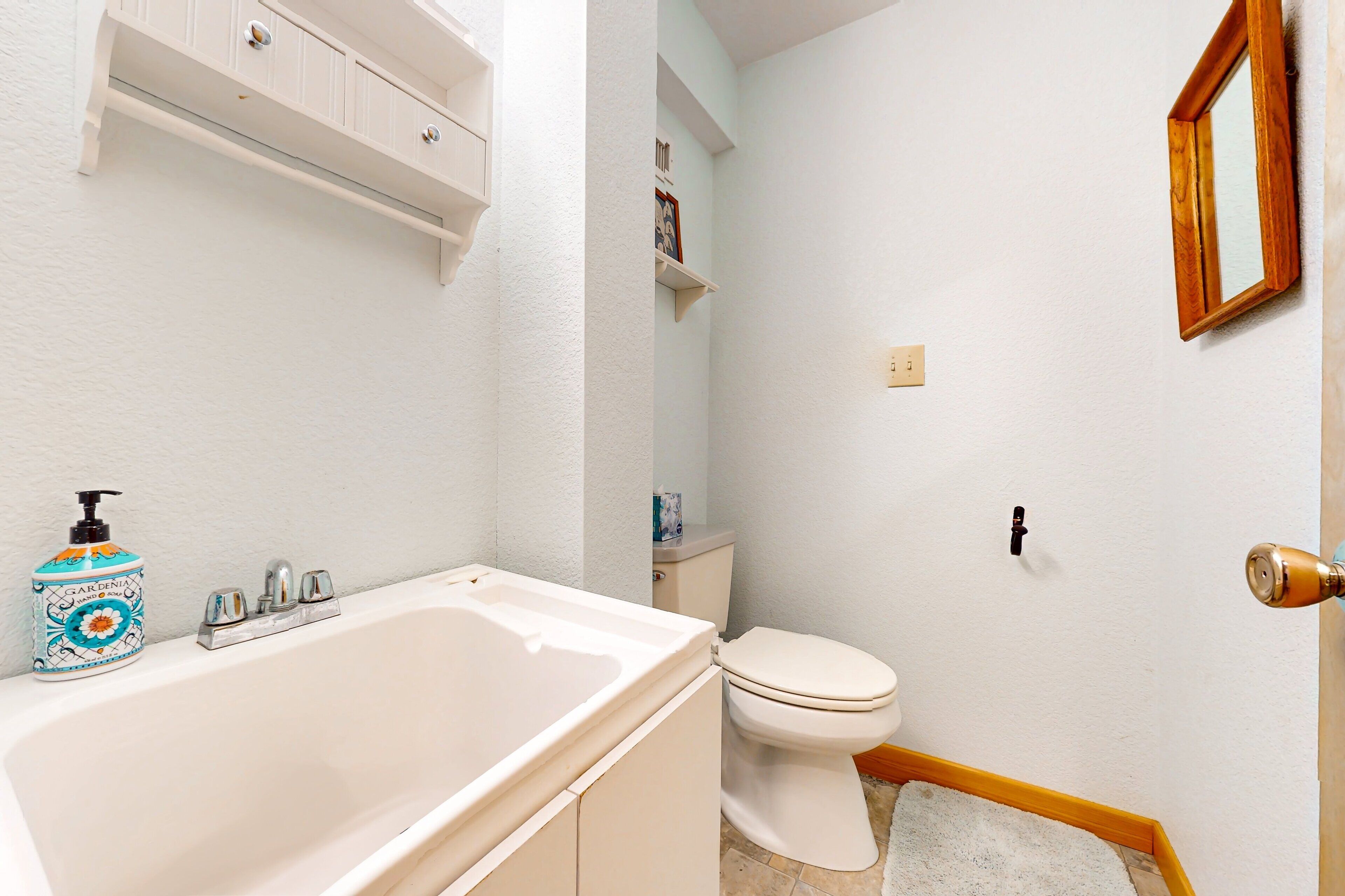 Un baño con una bañera blanca, un inodoro y un estante con artículos de aseo.