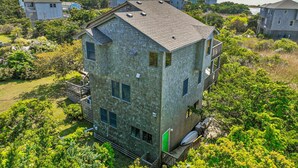 A multi-story building with a sloped roof, surrounded by lush greenery and other residential structures. - Shallow Point: Creek Views, Expansive decks and Full Kitchen! (Avon)