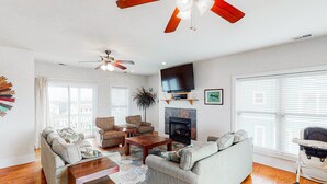 Un salon spacieux doté de planchers en bois franc, d’un ventilateur de plafond, d’une cheminée et d’un téléviseur.