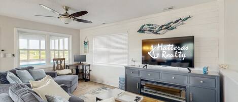 A living room with a gray sectional sofa, a wooden coffee table, a gray entertainment center, and a ceiling fan.
