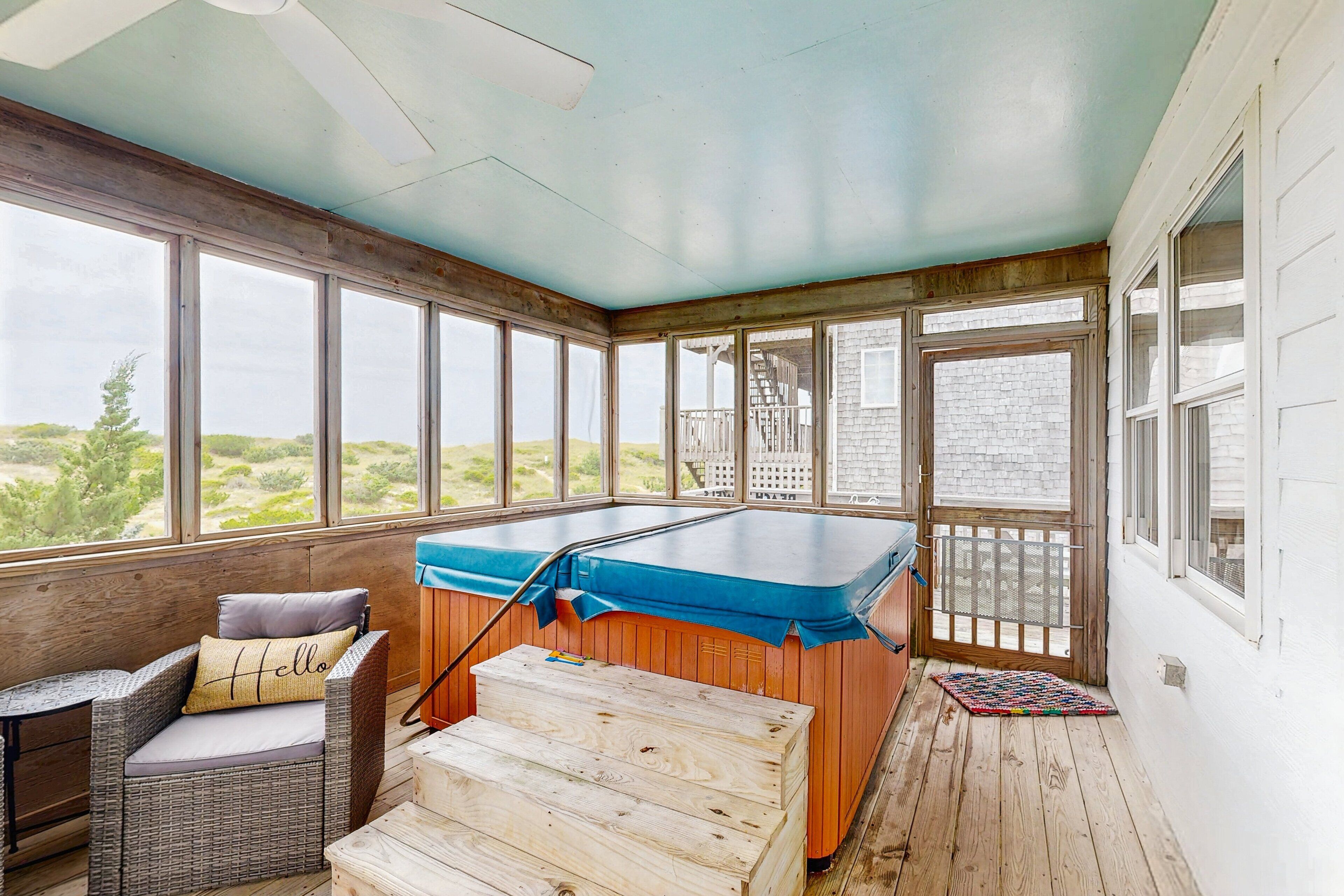 A sunroom with a pool table, a wicker chair, and large windows offering a view of the landscape.