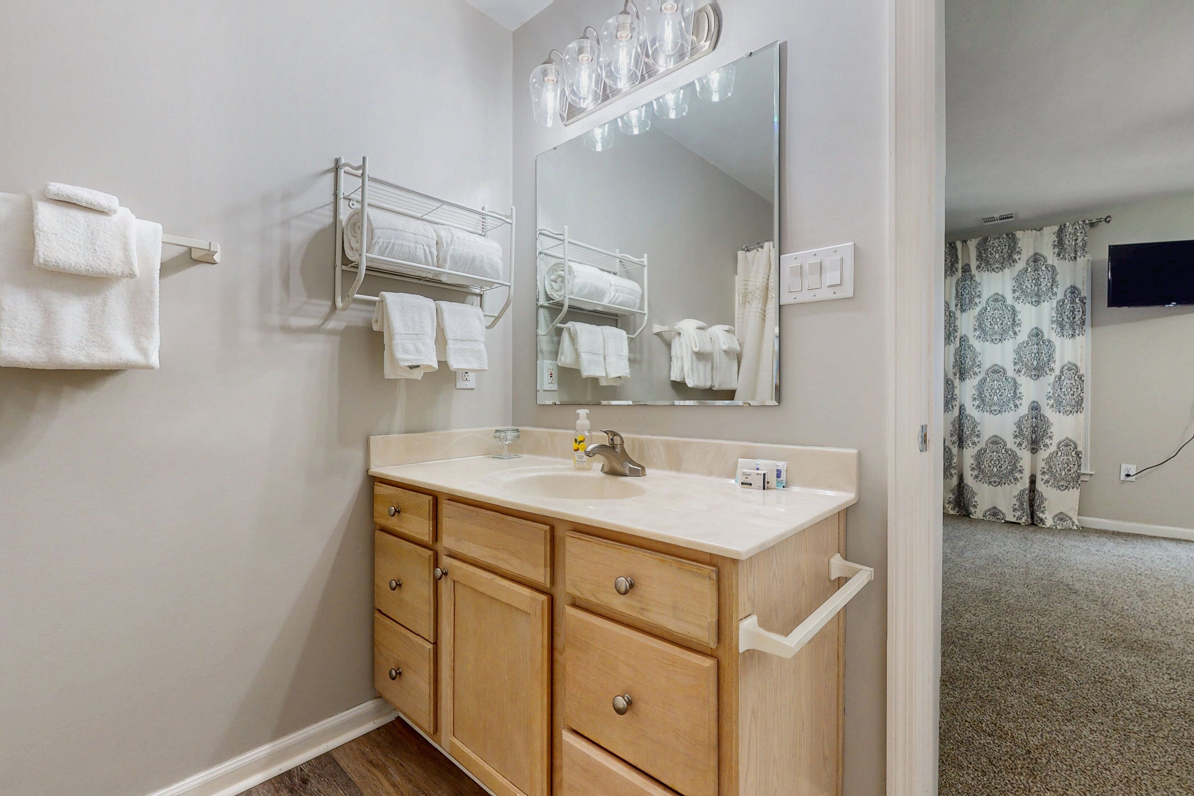 A bathroom with a wooden vanity, a large mirror, towel racks, and a shower curtain.