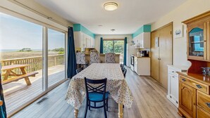 A dining area with a table and chairs, a wooden bench, and a view of the beach through large windows. - Classic home with sound & marsh views, hot tub, decks - near beaches/lighthouse (Frisco)