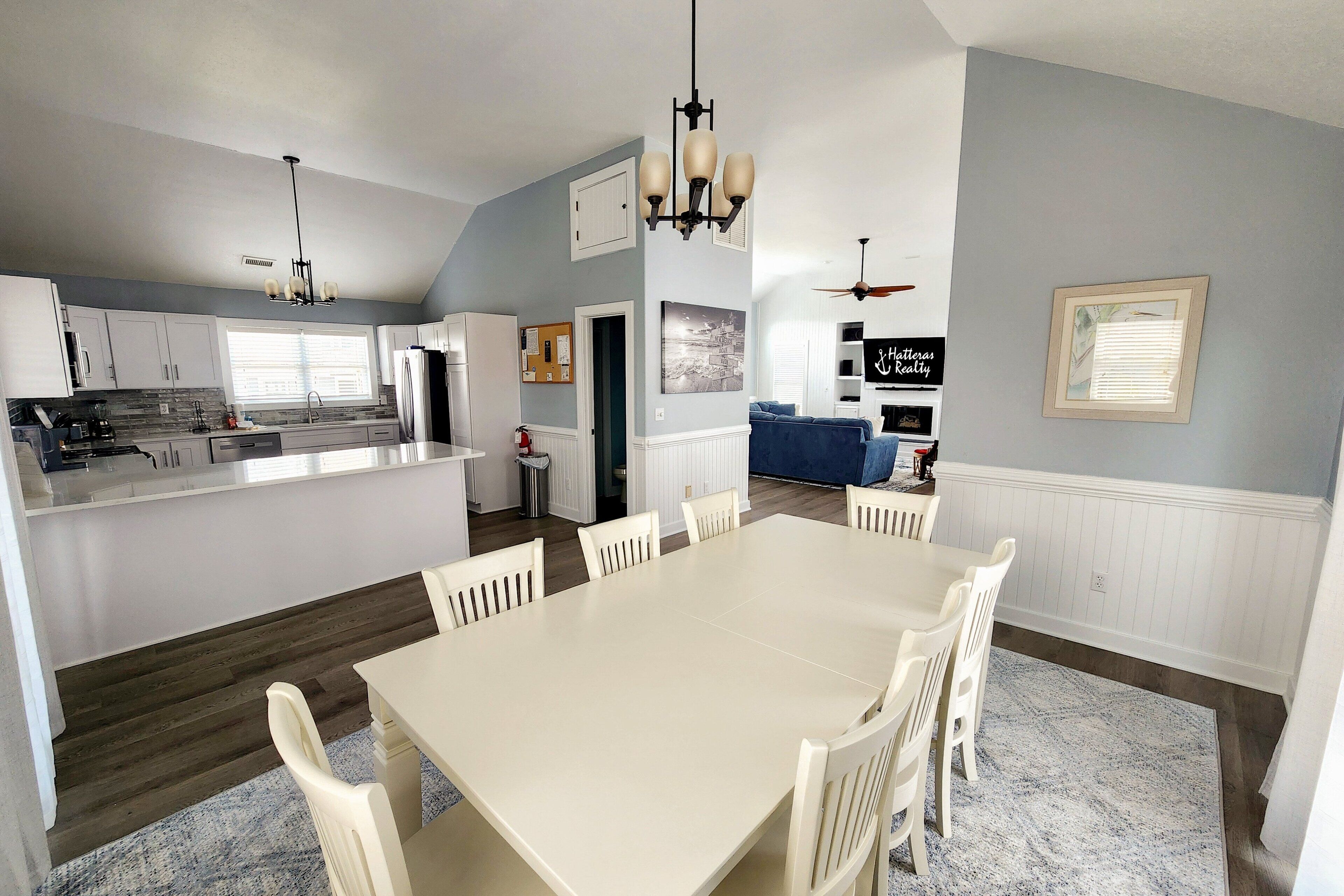A spacious kitchen with white cabinets, a central island, and a dining area with a white table and chairs.