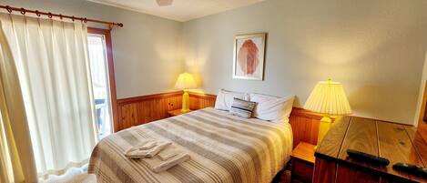 A bedroom with a bed, two bedside lamps, a ceiling fan, a window with curtains, and a framed picture on the wall.