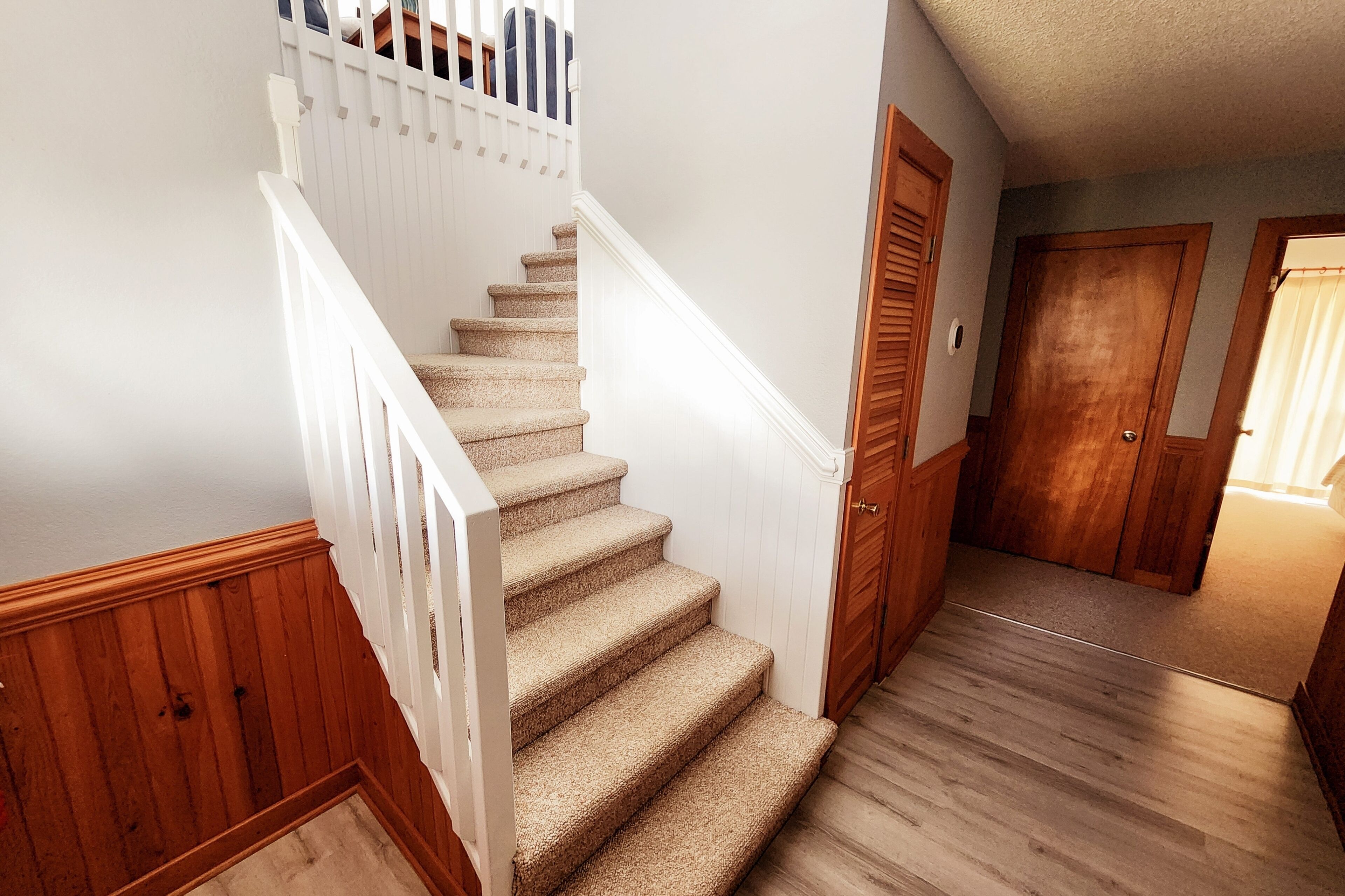 A staircase with wooden railings and carpeted steps leading to a landing.