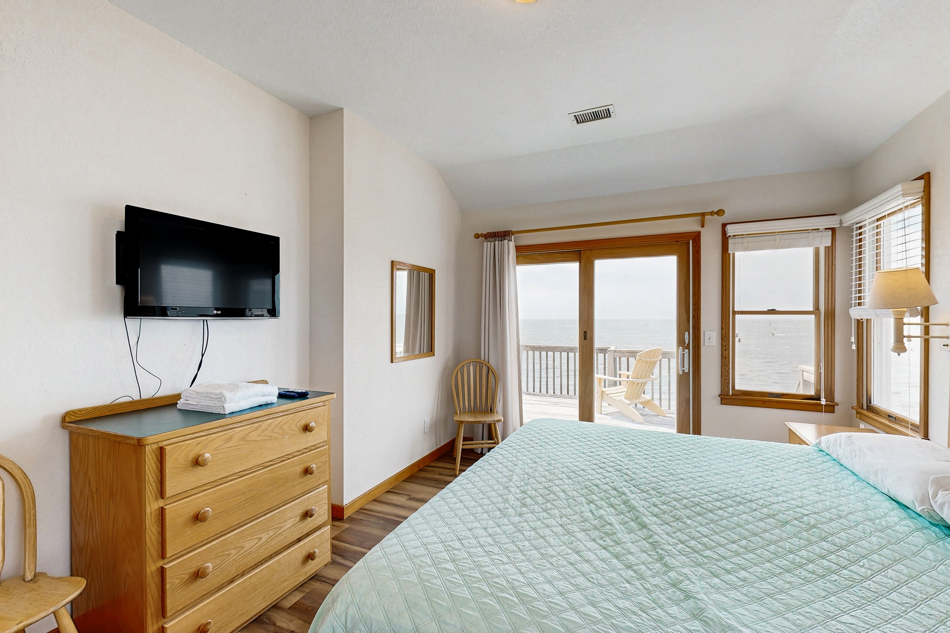 Une chambre à coucher comprenant un lit, une commode, un téléviseur, une chaise et un balcon avec vue sur la mer.